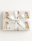 Flat lay of a gift wrapped in elegant wedding cake wrapping paper with tiered cakes and pink roses, tied with a white satin ribbon and bow