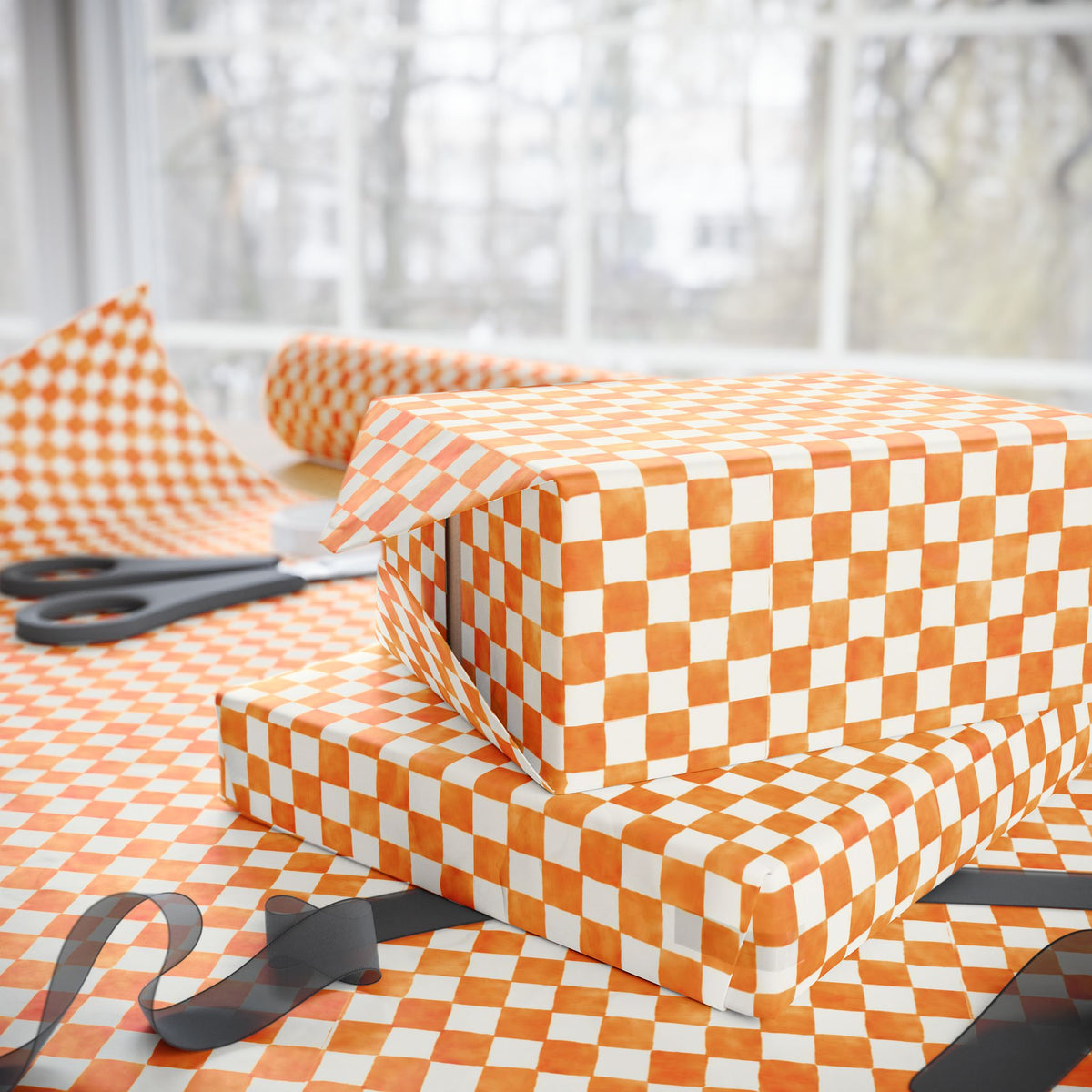 Orange and soft white checkered wrapping paper wrapped around two gift boxes, with scissors and ribbon on a table in front of a softly blurred window.