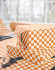 Orange and soft white checkered wrapping paper wrapped around two gift boxes, with scissors and ribbon on a table in front of a softly blurred window.