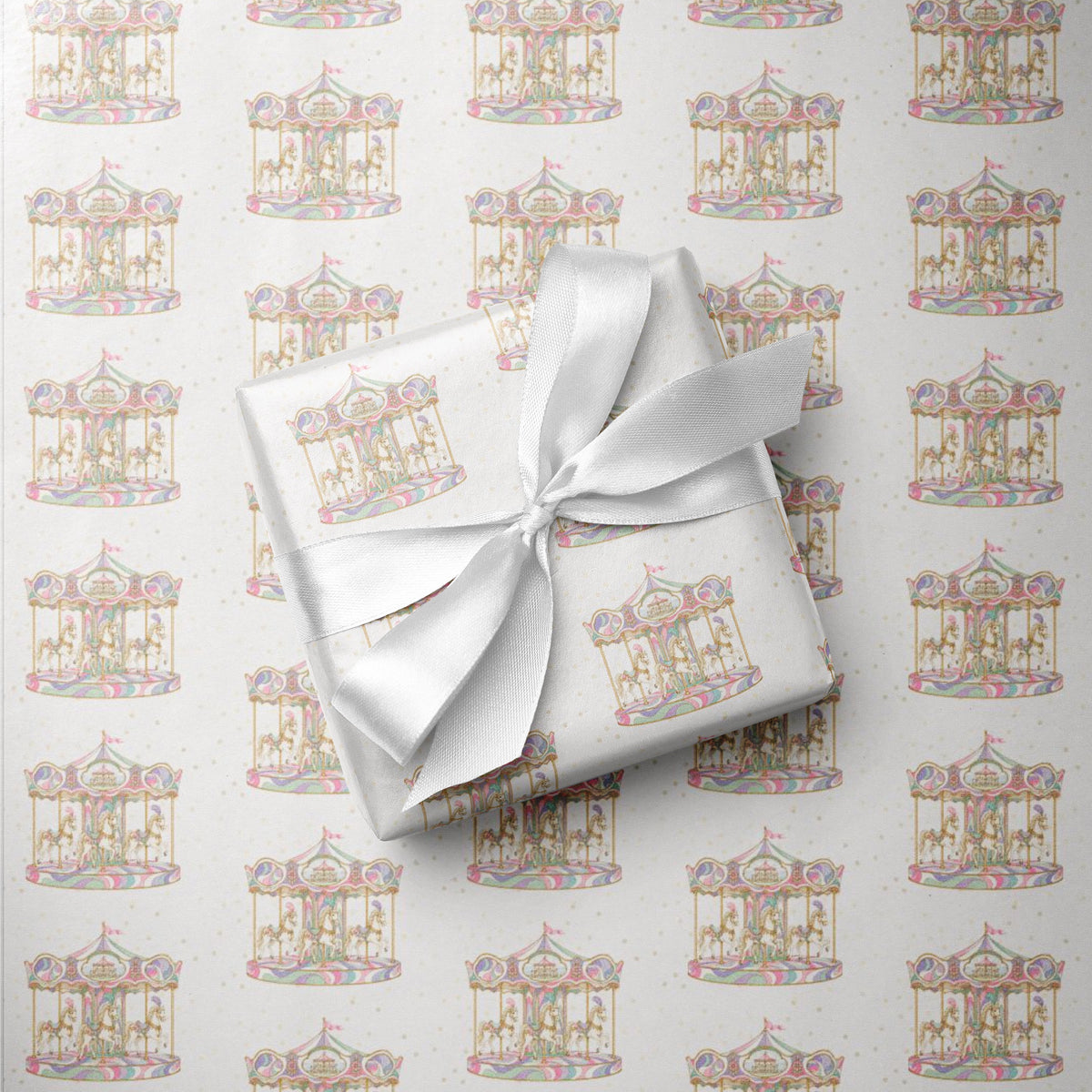 A gift box wrapped in white paper with a repeating carousel pattern, tied with a white satin ribbon, placed on top of matching patterned wrapping paper.