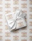 A gift box wrapped in white paper with a repeating carousel pattern, tied with a white satin ribbon, placed on top of matching patterned wrapping paper.