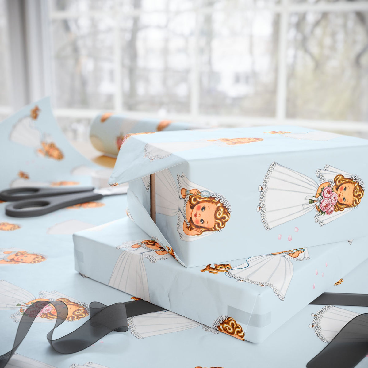 Light blue wrapping paper with a illustrations of a vintage bride, shown wrapped around gift boxes on a table with scissors and ribbon in a bright indoor setting.