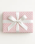 A rectangular gift box wrapped in pink and white checkered wrapping paper with a white satin ribbon tied in a bow, photographed from above on a clean white background.