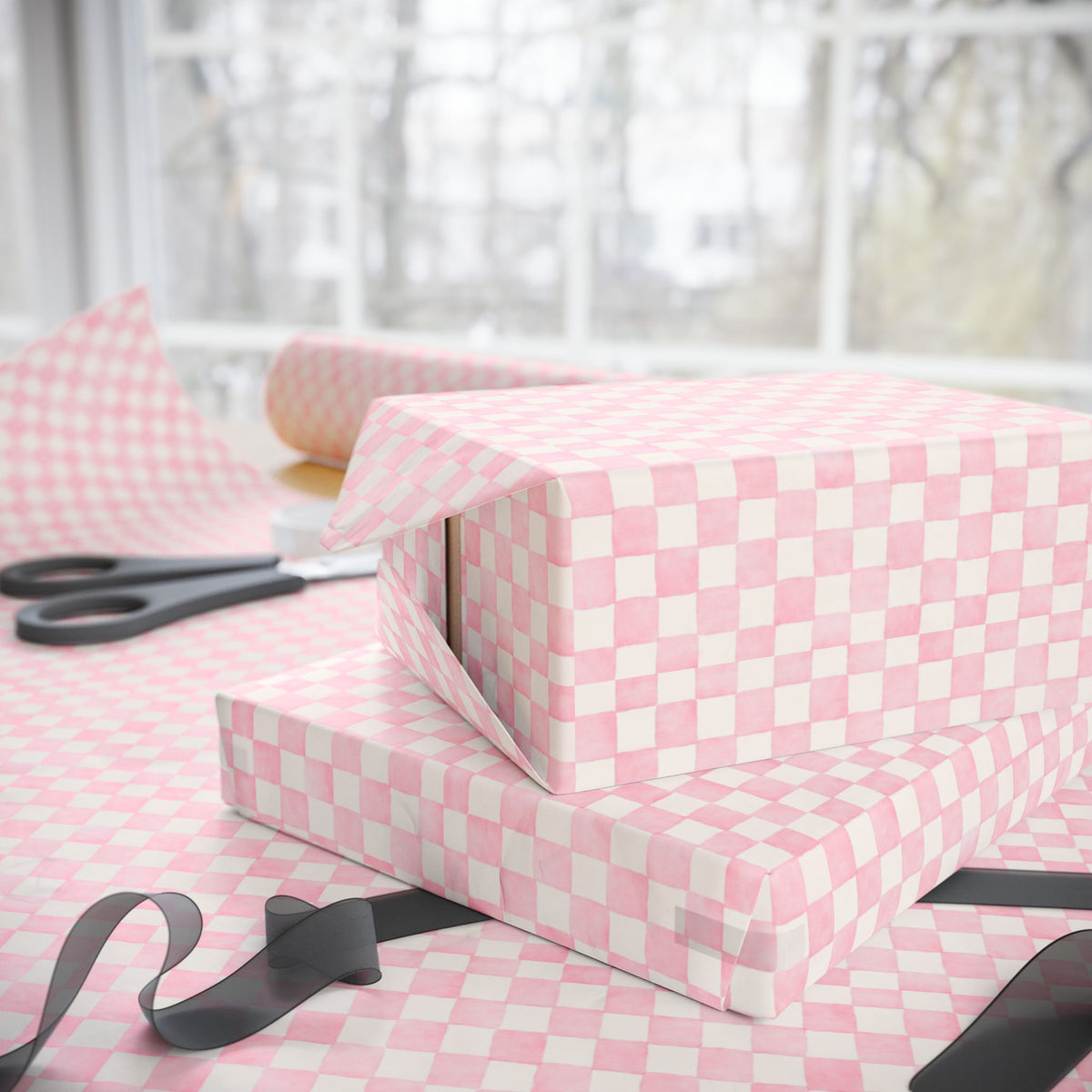 Pink and white checkered wrapping paper displayed on a table with a gift box, scissors, and ribbon in a softly lit room.