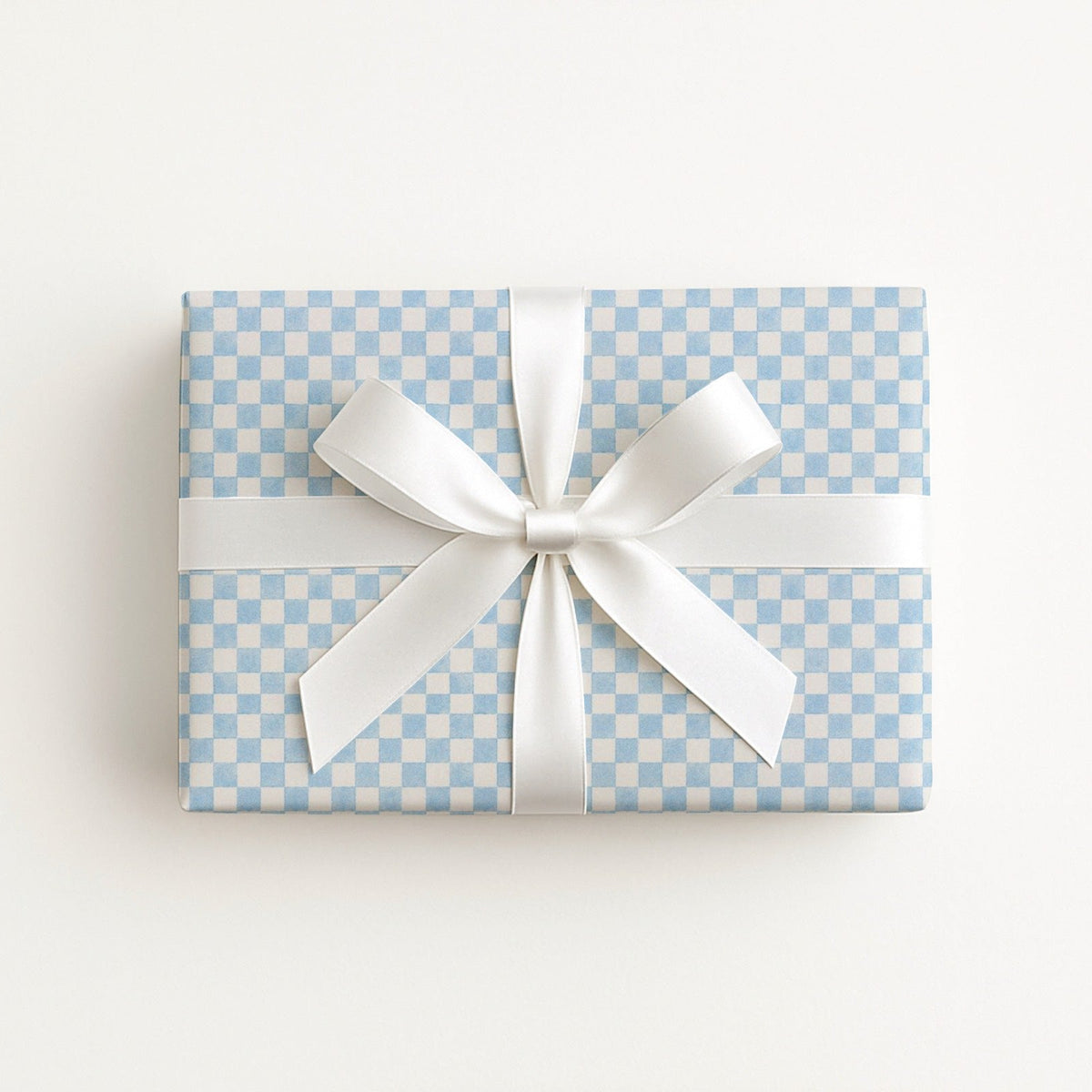 A rectangular gift box wrapped in light blue and white checkered paper, tied with a wide white satin ribbon and bow, photographed from above on a clean white background.