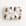 A rectangular gift box wrapped in white paper featuring a repeating pattern of vintage-style illustrated bride and groom, tied with a large white satin bow in the center, on a plain white background.
