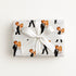 A rectangular gift box wrapped in white paper featuring a repeating pattern of vintage-style illustrated bride and groom, tied with a large white satin bow in the center, on a plain white background.
