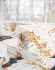Wrapped presents in retro giraffe baby girl wrapping paper on a gift wrapping table with scissors and ribbon by a sunny window