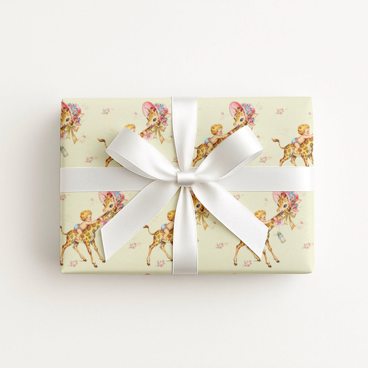 Vintage-style safari giraffe baby boy wrapping paper on a gift tied with a white satin bow, baby boys riding giraffes in floral bonnets on butter yellow