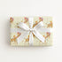 Vintage-style safari giraffe baby boy wrapping paper on a gift tied with a white satin bow, baby boys riding giraffes in floral bonnets on butter yellow
