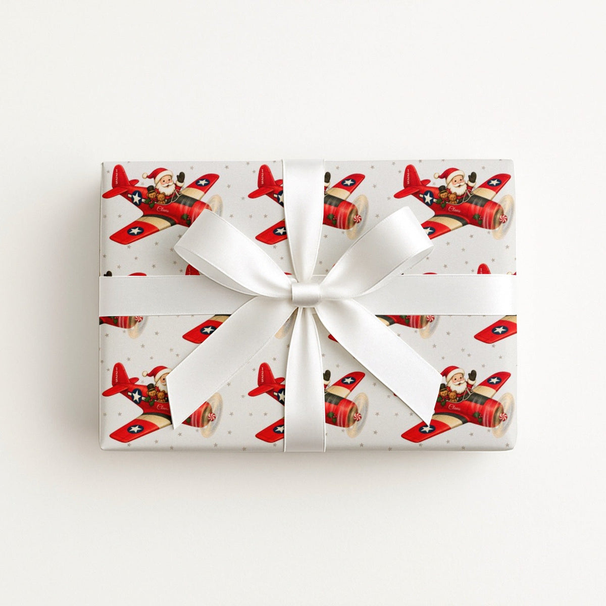 A rectangular gift box wrapped in Santa airplane Christmas wrapping paper with red propeller plane.