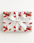 A rectangular gift box wrapped in Santa airplane Christmas wrapping paper with red propeller plane.