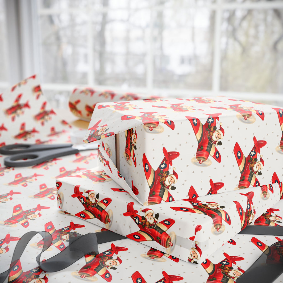 Christmas-themed wrapping paper with a red airplane pattern featuring Santa Claus, shown wrapped around gift boxes on a table with scissors and ribbon near a window.