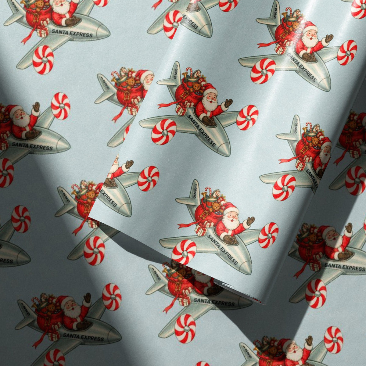 Light blue wrapping paper with a repeating pattern of Santa Claus in a silver Santa Express airplane, surrounded by red and white peppermint candies.