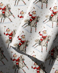 Christmas wrapping paper with a repeating vintage style illustration of Santa Claus riding a polo pony, shown with one roll partially unrolled over the other.