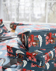 Holiday-themed wrapping paper with Santa Claus, a red train and candy cane pattern on a navy background, shown wrapped around gift boxes on a table with scissors and wrapping ribbon near a window.