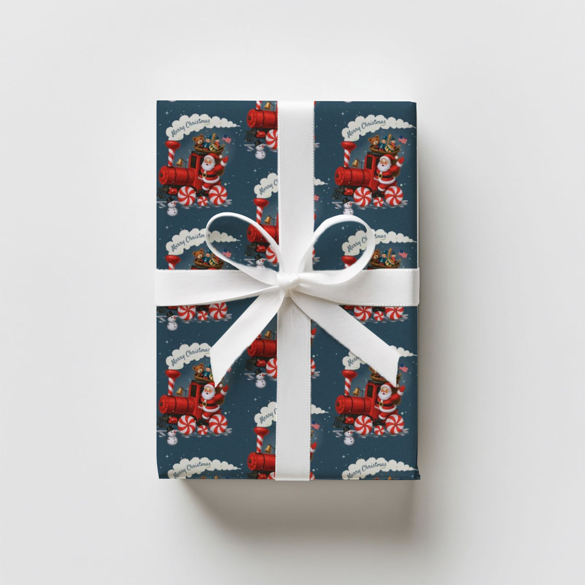 A rectangular gift box wrapped in dark blue holiday paper with a red Santa train and candy cane pattern, tied with a white ribbon and bow.