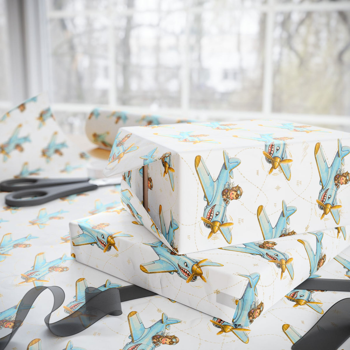 Ivory wrapping paper with a repeating pattern of vintage blue and gold airplanes, shown wrapped around gift boxes on a table with scissors and ribbon nearby.