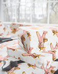 Ivory wrapping paper with a repeating pattern of vintage pink and gold airplanes, shown wrapped around gift boxes on a table with scissors and ribbon nearby.