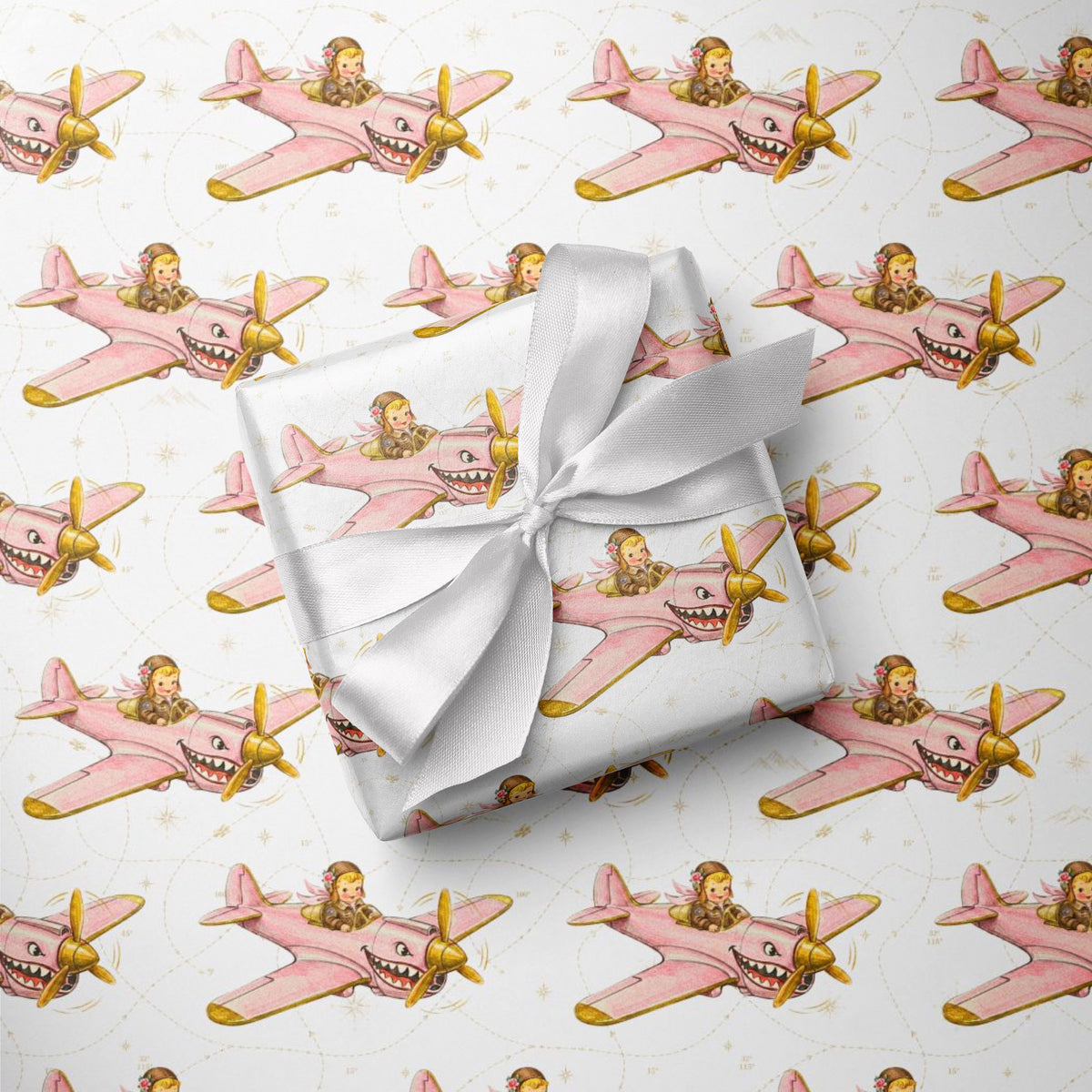 Wrapped gift tied with a white satin bow, displayed on matching wrapping paper featuring a little girl flying a pink warplane with a painted shark mouth over a delicate navigation map with gold accents on an ivory background.