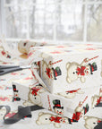 Ivory wrapping paper with a repeating pattern of vintage illustrated snowmen, styled on a table with scissors and gift boxes in a bright room.
