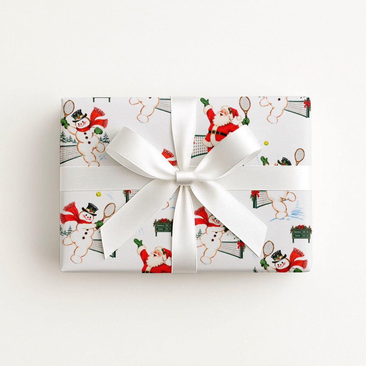 Flat lay of a gift wrapped in vintage-style Santa and snowman tennis Christmas wrapping paper with a white satin bow