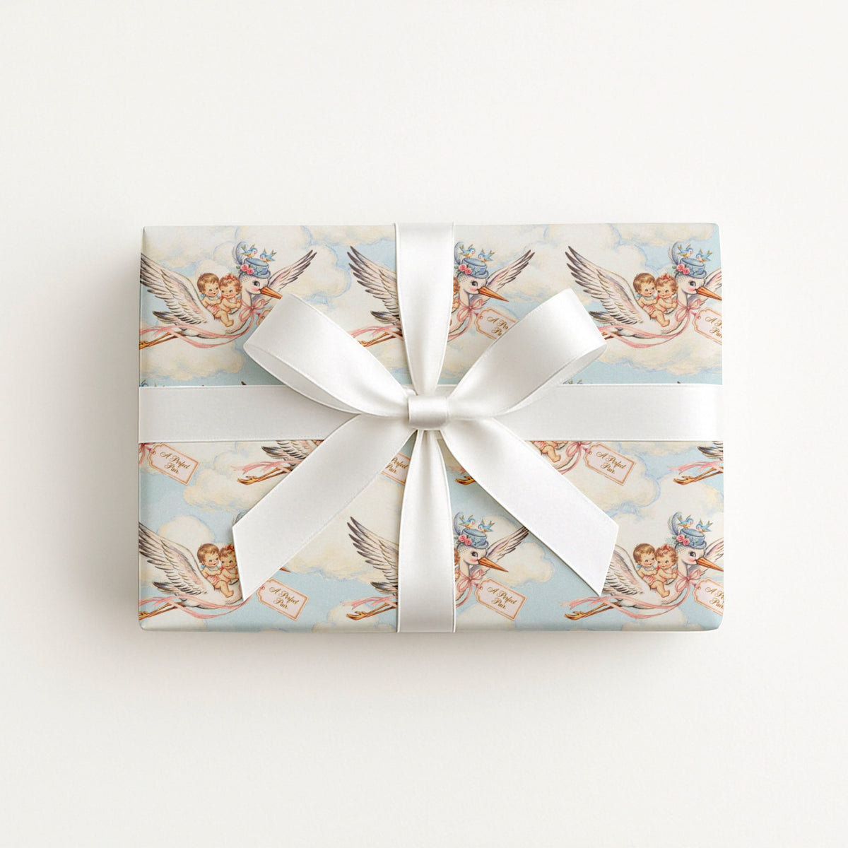 Flat lay of a gift wrapped in vintage-style twin baby shower wrapping paper with storks and a white satin bow