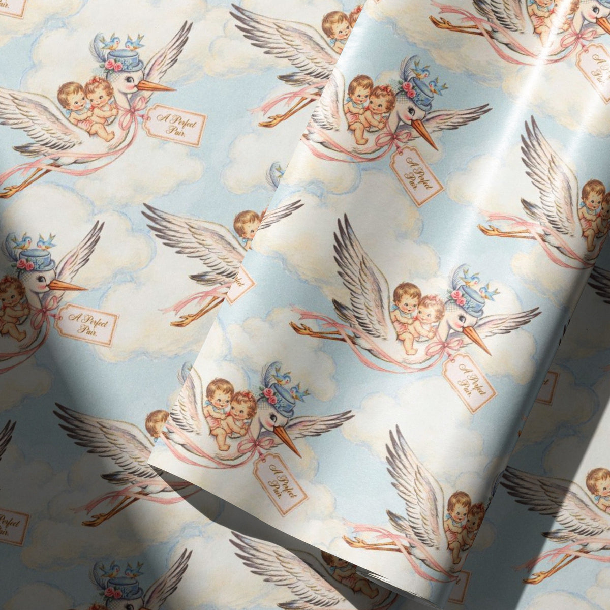 Vintage-style twin baby shower wrapping paper with a baby boy and girl riding a stork through soft blue clouds, shown as a roll in soft light