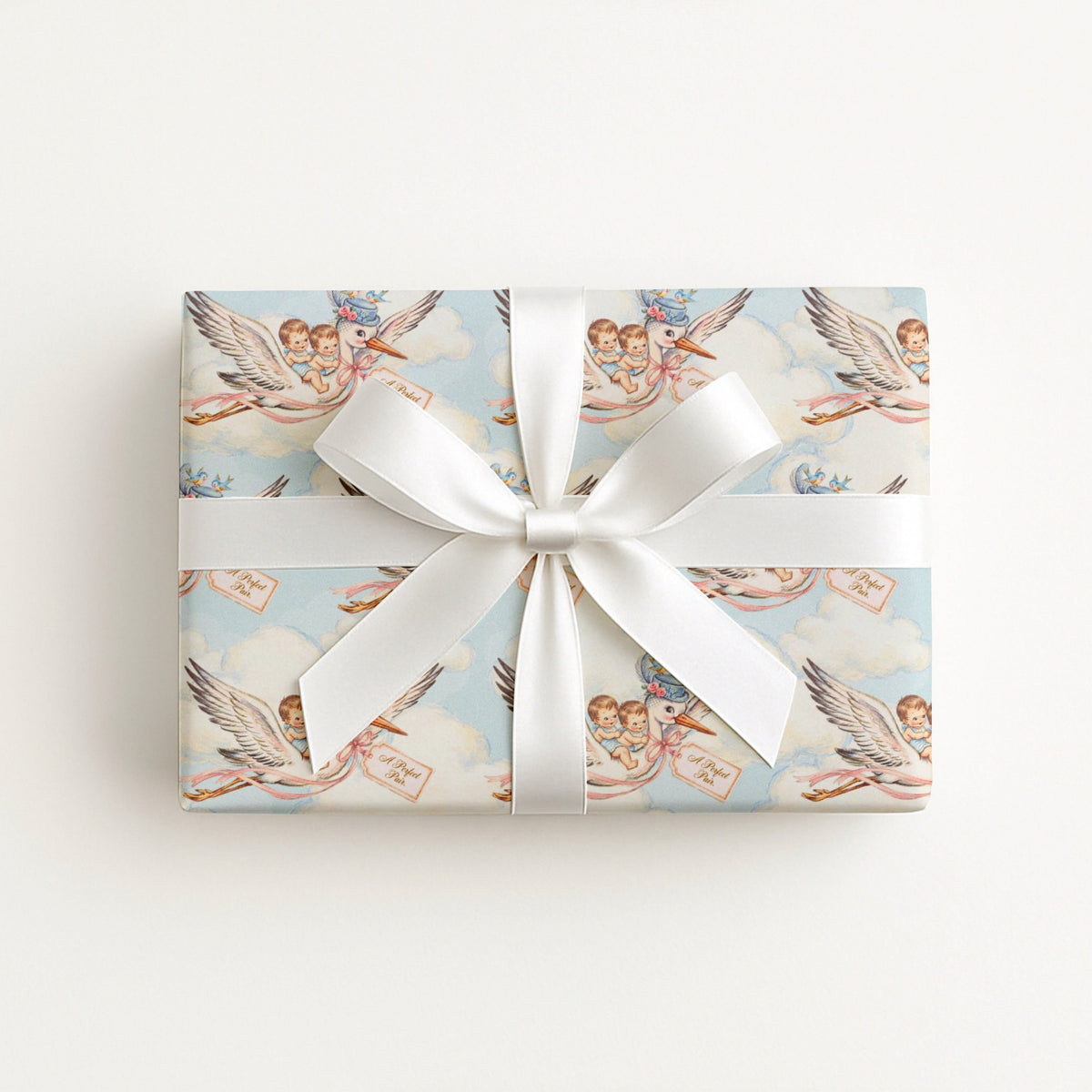 Twin boys stork wrapping paper on a gift tied with a white satin bow