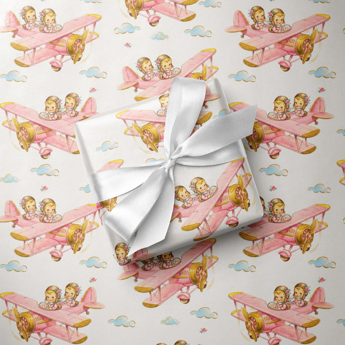 Flat lay of twin girl airplane wrapping paper with a wrapped gift tied with a white satin ribbon.