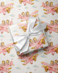 Flat lay of twin girl airplane wrapping paper with a wrapped gift tied with a white satin ribbon.