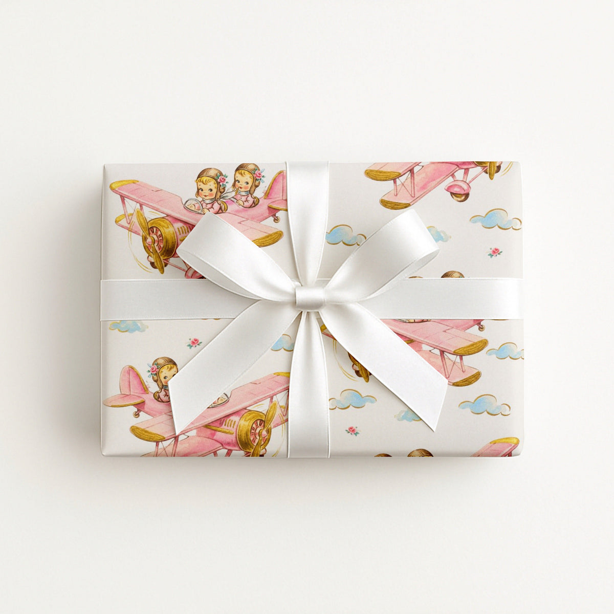 Twin girl airplane wrapping paper featuring two little aviators flying in a pastel pink vintage biplane.
