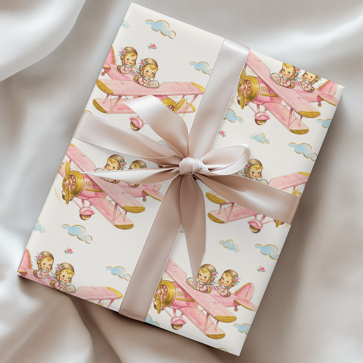 Wrapped gift featuring twin girls flying a pink biplane tied with a blush satin ribbon.