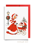 Vintage-style twins first Christmas card: a woman in a red coat trimmed with white fur pushes a pram with two sleepy babies past a wreath-trimmed lamppost, shown with a red envelope, Double the Joy twin baby shower card