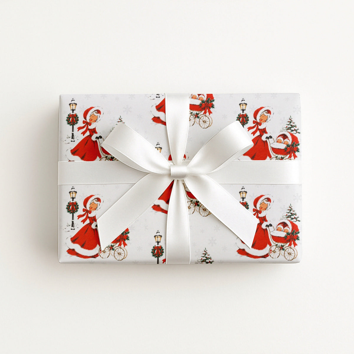 Gift wrapped in vintage-style twins first Christmas wrapping paper with a woman in a red coat trimmed with white fur pushing a pram with two sleepy babies, tied with a white satin ribbon bow, Double the Joy twin baby shower gift wrap