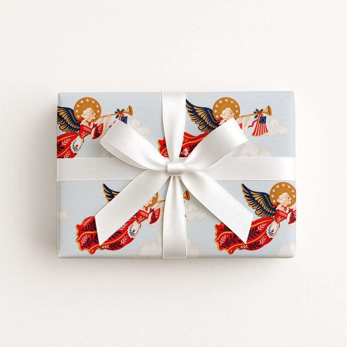 Flat lay of a gift wrapped in vintage-style patriotic angel Christmas wrapping paper with trumpet angels and a white satin bow