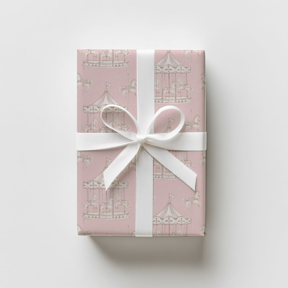 A rectangular gift box wrapped in blush pink vintage inspired carousel horse wrapping paper, beautifully tied with a wide white satin ribbon.