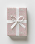 A rectangular gift box wrapped in blush pink vintage inspired carousel horse wrapping paper, beautifully tied with a wide white satin ribbon.