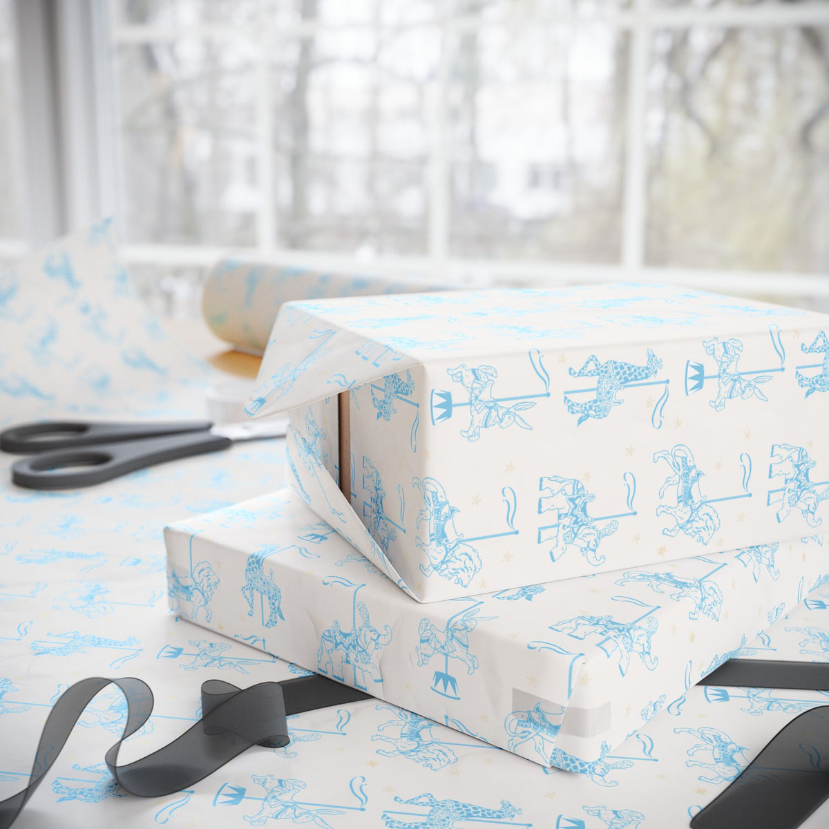 Ivory wrapping paper with a light blue carousel animal pattern, shown wrapped around stacked gift boxes on a table with scissors and ribbon near a bright window.