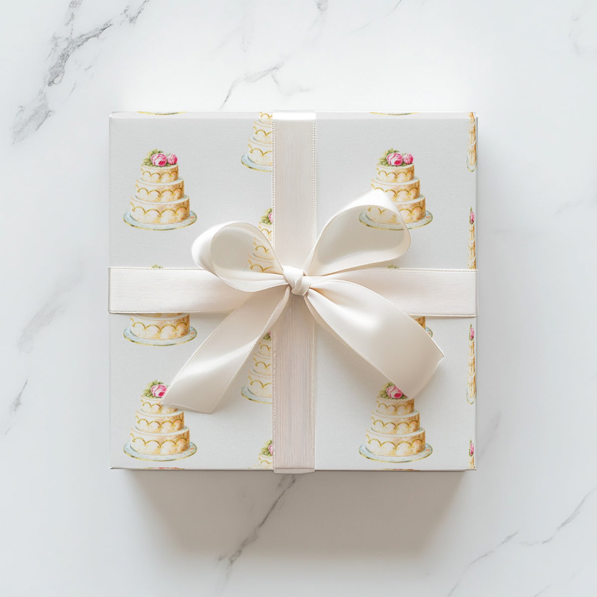 Square wedding gift wrapped in elegant ivory wedding cake wrapping paper with a cream satin bow on a white marble surface